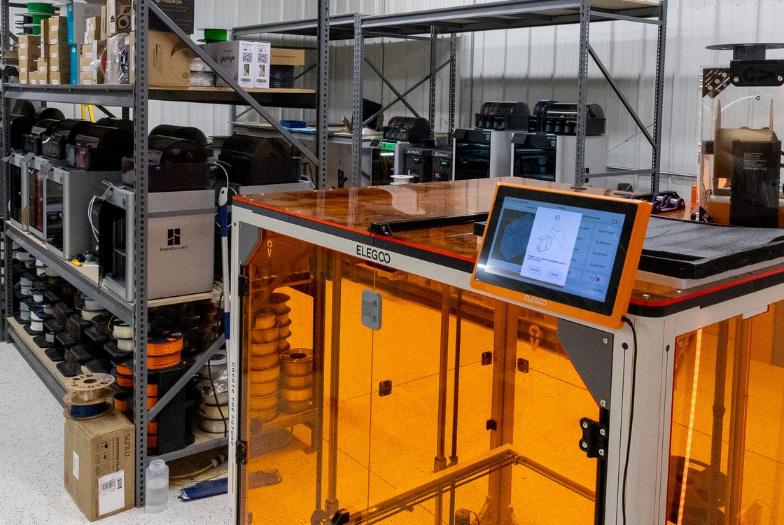 Large format FDM printer running beside racks of filament on the Variety Vault shop floor in Ames, Iowa